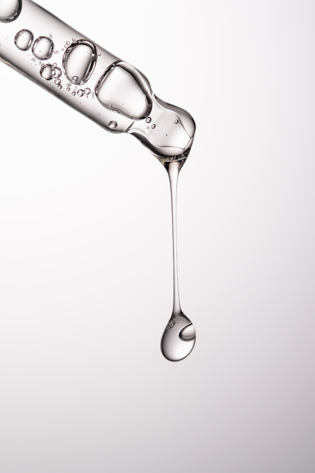 Close-up of a dropper with liquid dripping against a light gray background